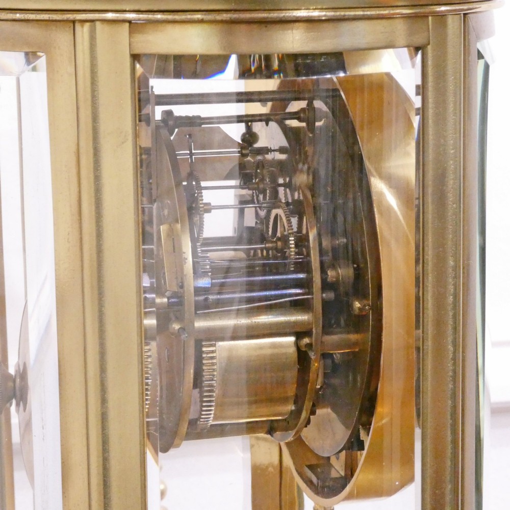 A French gilt bronze and brass four-glass mantel clock featuring an urn finial, visible pendulum mechanism, and white enamel dial with Roman numerals. View XIII