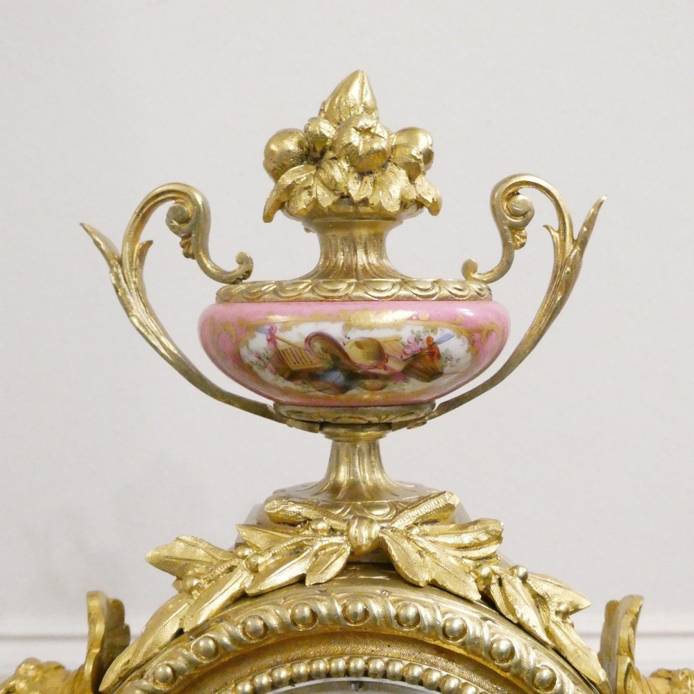 A Louis XVI style gilt bronze mantel clock featuring hand-painted pink porcelain panels and an urn-shaped finial. View VI