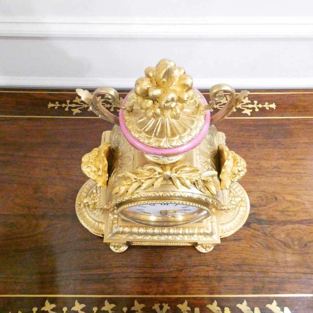 A Louis XVI style gilt bronze mantel clock featuring hand-painted pink porcelain panels and an urn-shaped finial. View VIII