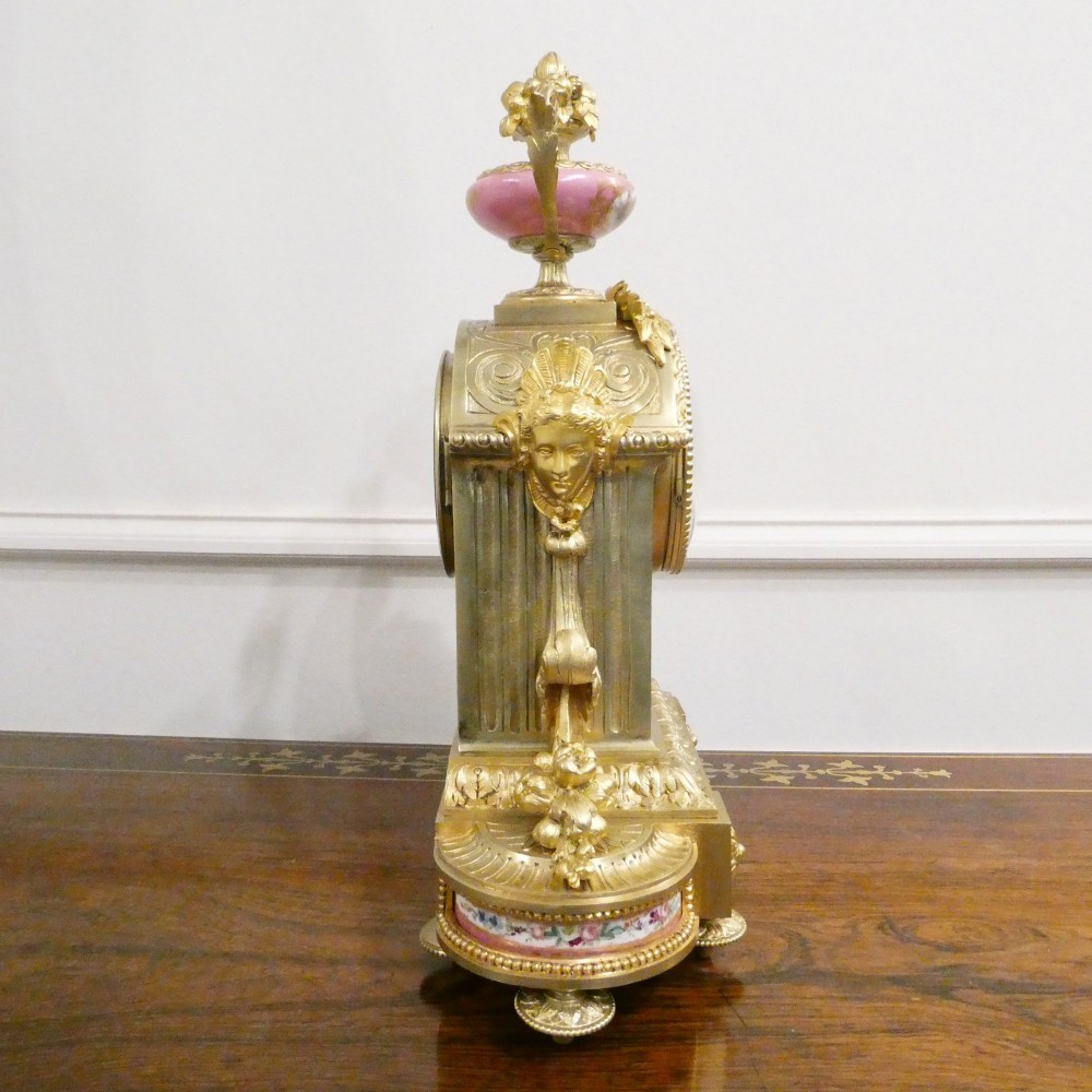 A Louis XVI style gilt bronze mantel clock featuring hand-painted pink porcelain panels and an urn-shaped finial. View IX