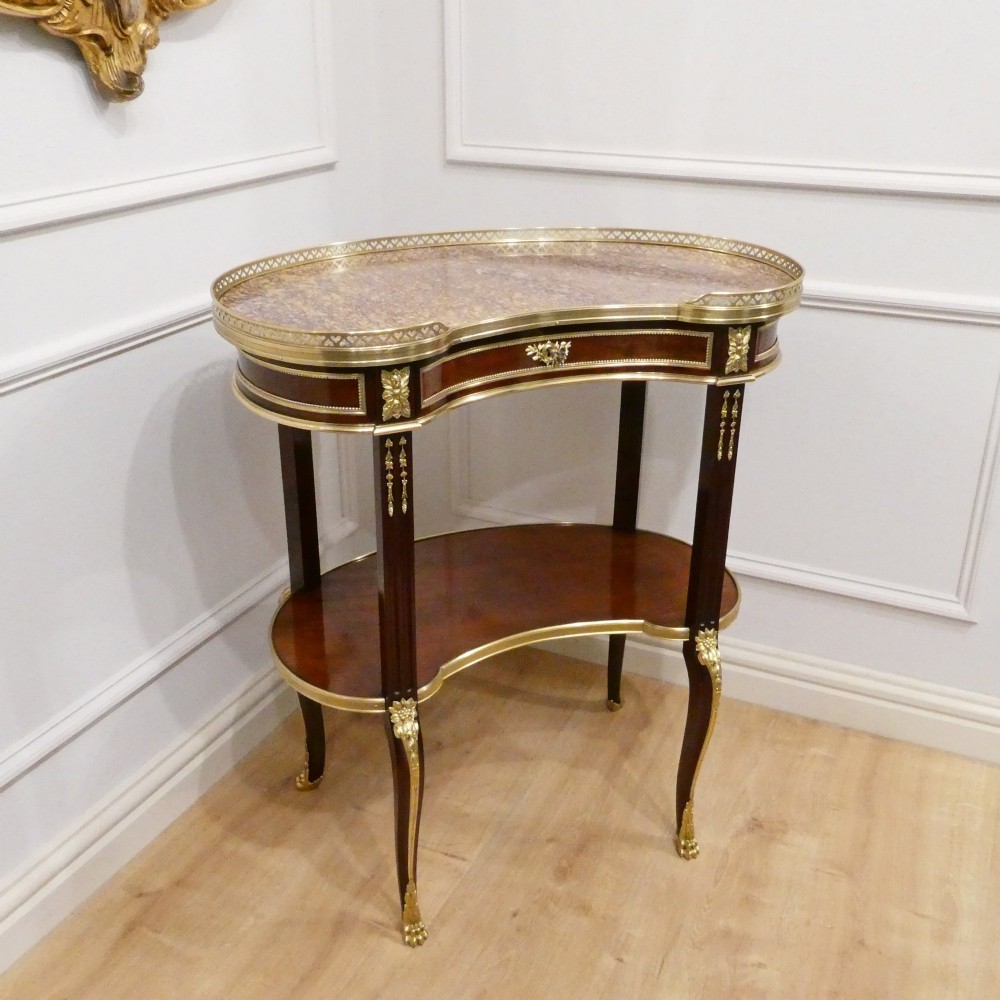 A French Louis XVI style kidney-shaped mahogany side table featuring a marble top, pierced brass gallery, lower undertier, and elaborate gilt-bronze mounts.