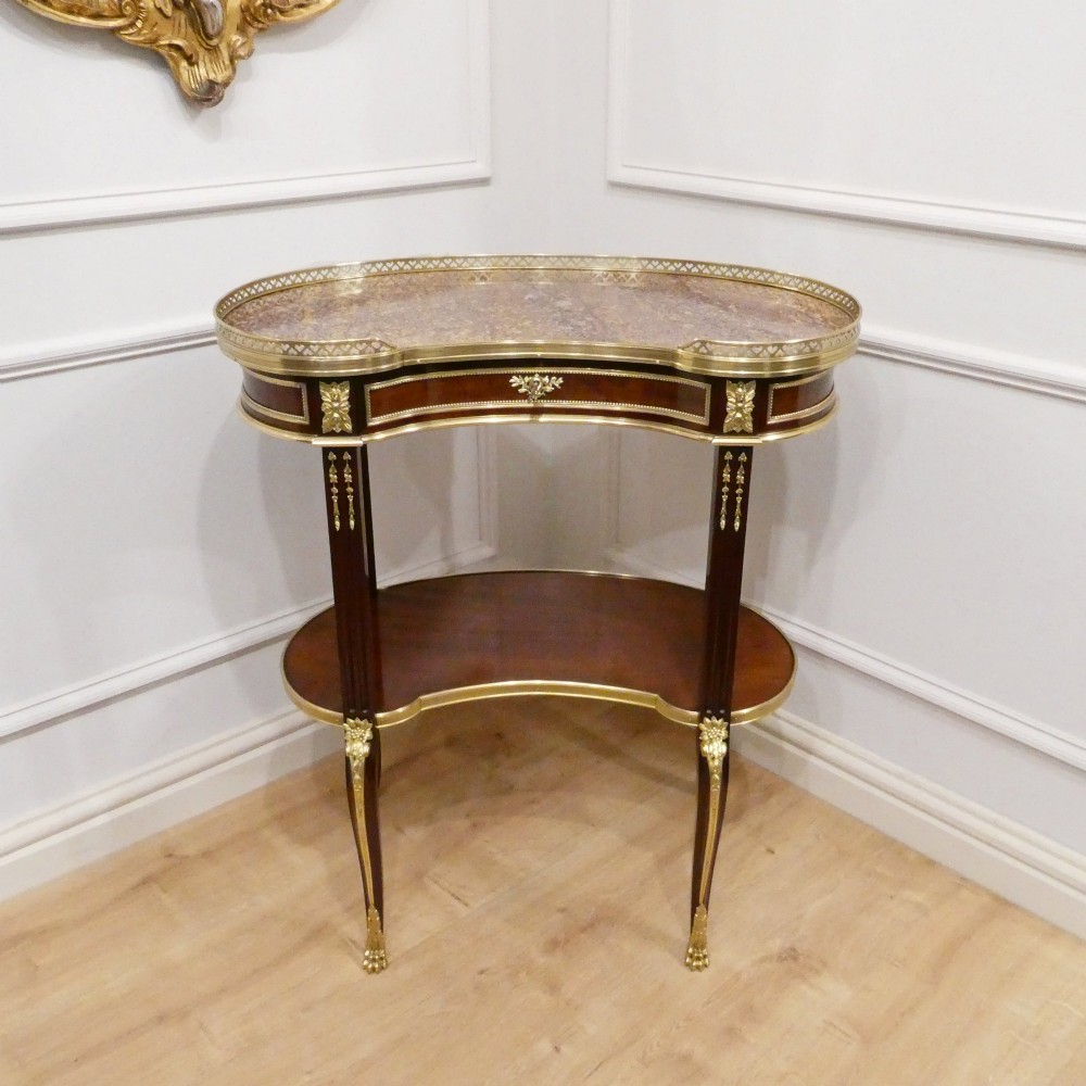 A French Louis XVI style kidney-shaped mahogany side table featuring a marble top, pierced brass gallery, lower undertier, and elaborate gilt-bronze mounts. View II