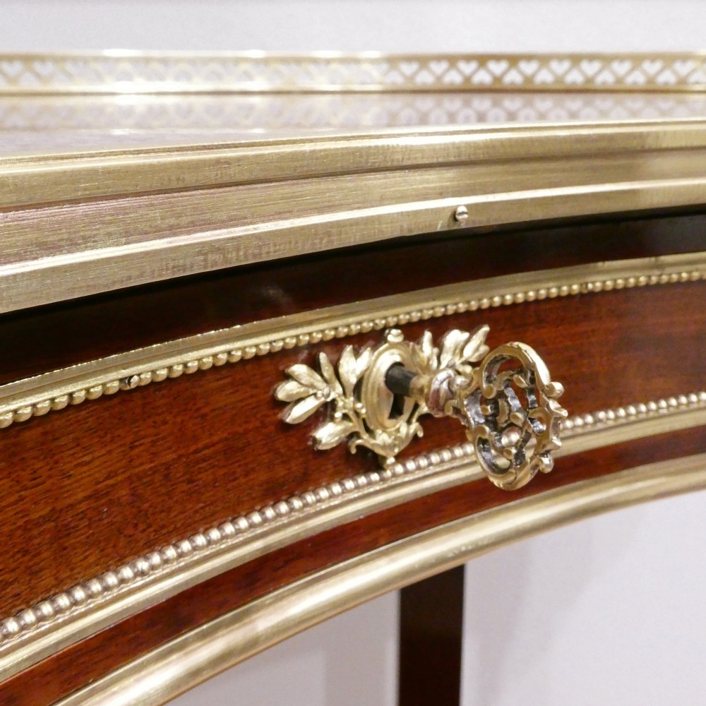 A French Louis XVI style kidney-shaped mahogany side table featuring a marble top, pierced brass gallery, lower undertier, and elaborate gilt-bronze mounts. View III