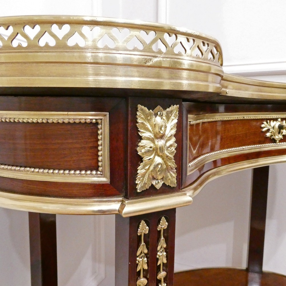 A French Louis XVI style kidney-shaped mahogany side table featuring a marble top, pierced brass gallery, lower undertier, and elaborate gilt-bronze mounts. View IV