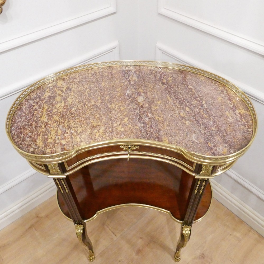 A French Louis XVI style kidney-shaped mahogany side table featuring a marble top, pierced brass gallery, lower undertier, and elaborate gilt-bronze mounts. View V