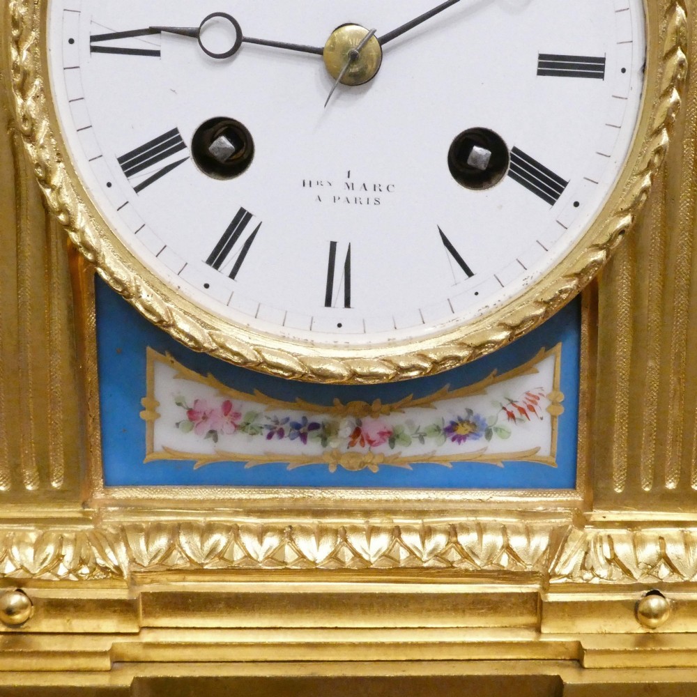 A French Louis XVI style gilt bronze mantel clock featuring a top urn finial, fluted side columns, and hand-painted blue porcelain panels around a white enamel dial. View V