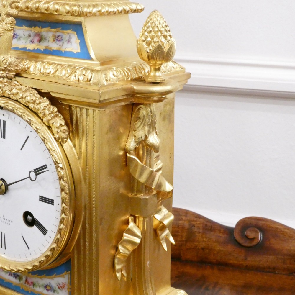 A French Louis XVI style gilt bronze mantel clock featuring a top urn finial, fluted side columns, and hand-painted blue porcelain panels around a white enamel dial. View VII