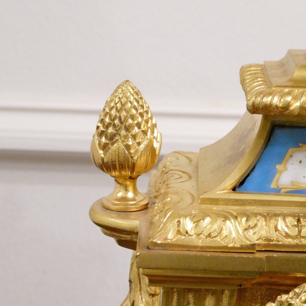 A French Louis XVI style gilt bronze mantel clock featuring a top urn finial, fluted side columns, and hand-painted blue porcelain panels around a white enamel dial. View IX