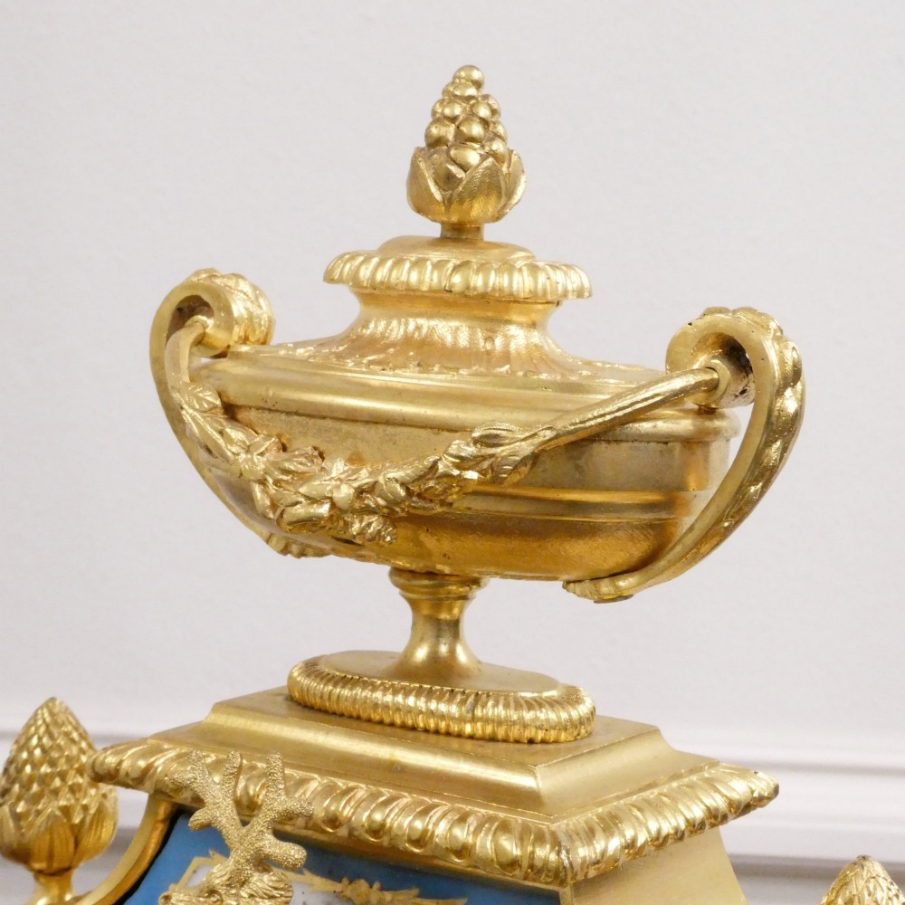 A French Louis XVI style gilt bronze mantel clock featuring a top urn finial, fluted side columns, and hand-painted blue porcelain panels around a white enamel dial. View X