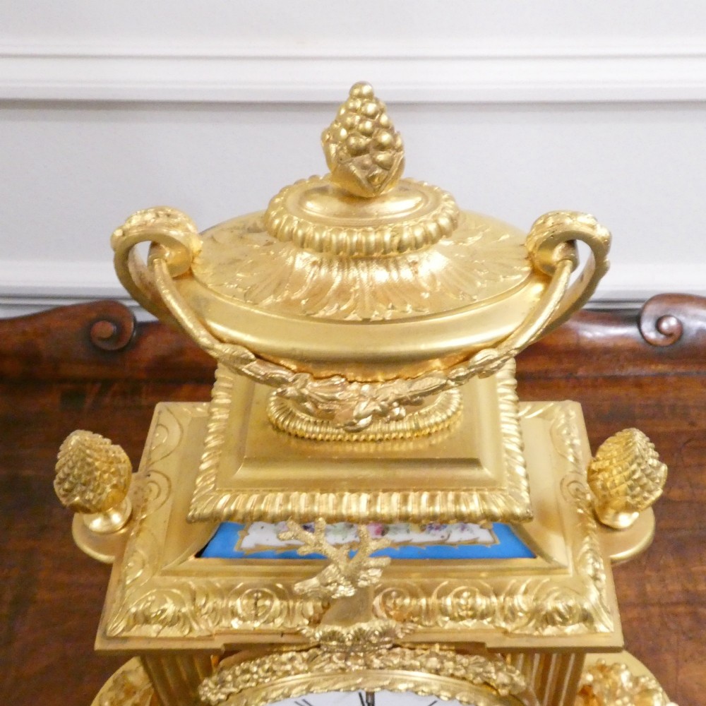 A French Louis XVI style gilt bronze mantel clock featuring a top urn finial, fluted side columns, and hand-painted blue porcelain panels around a white enamel dial. View XI