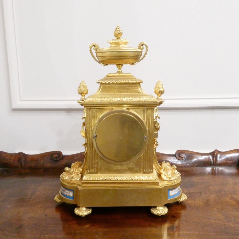 A French Louis XVI style gilt bronze mantel clock featuring a top urn finial, fluted side columns, and hand-painted blue porcelain panels around a white enamel dial. View XIII