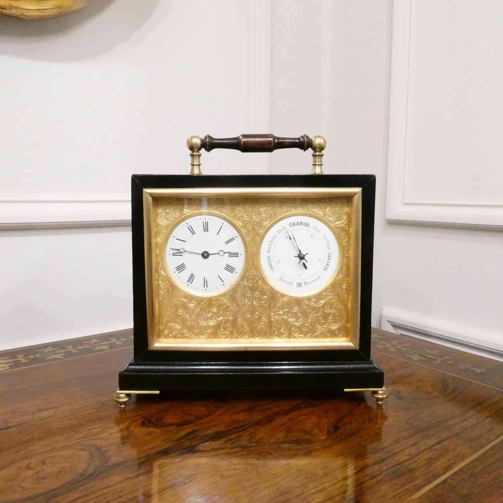 An Edwardian rectangular ebonised wooden mantel clock and barometer unit with twin white circular dials set into a scroll-engraved brass plate.