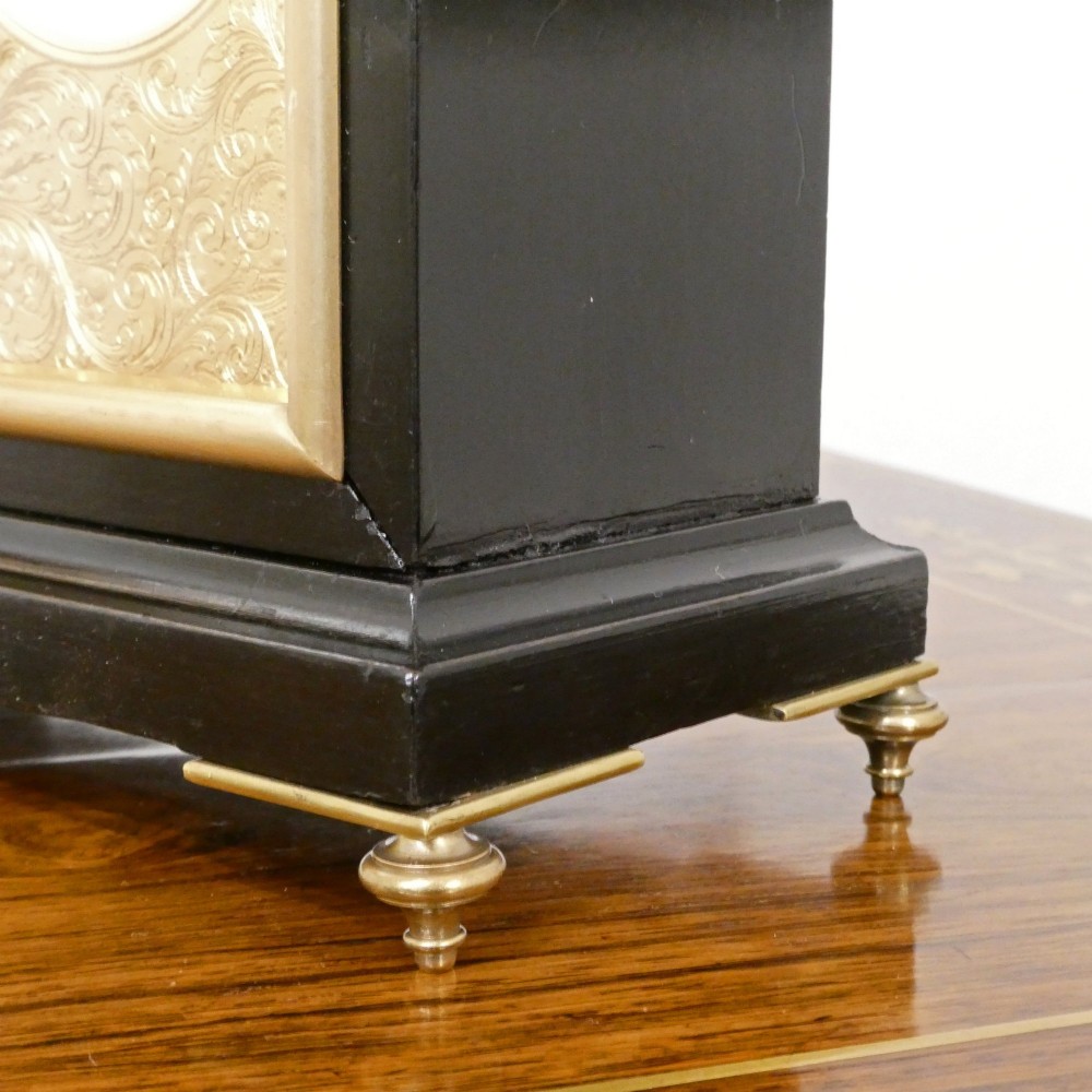 An Edwardian rectangular ebonised wooden mantel clock and barometer unit with twin white circular dials set into a scroll-engraved brass plate. View IX