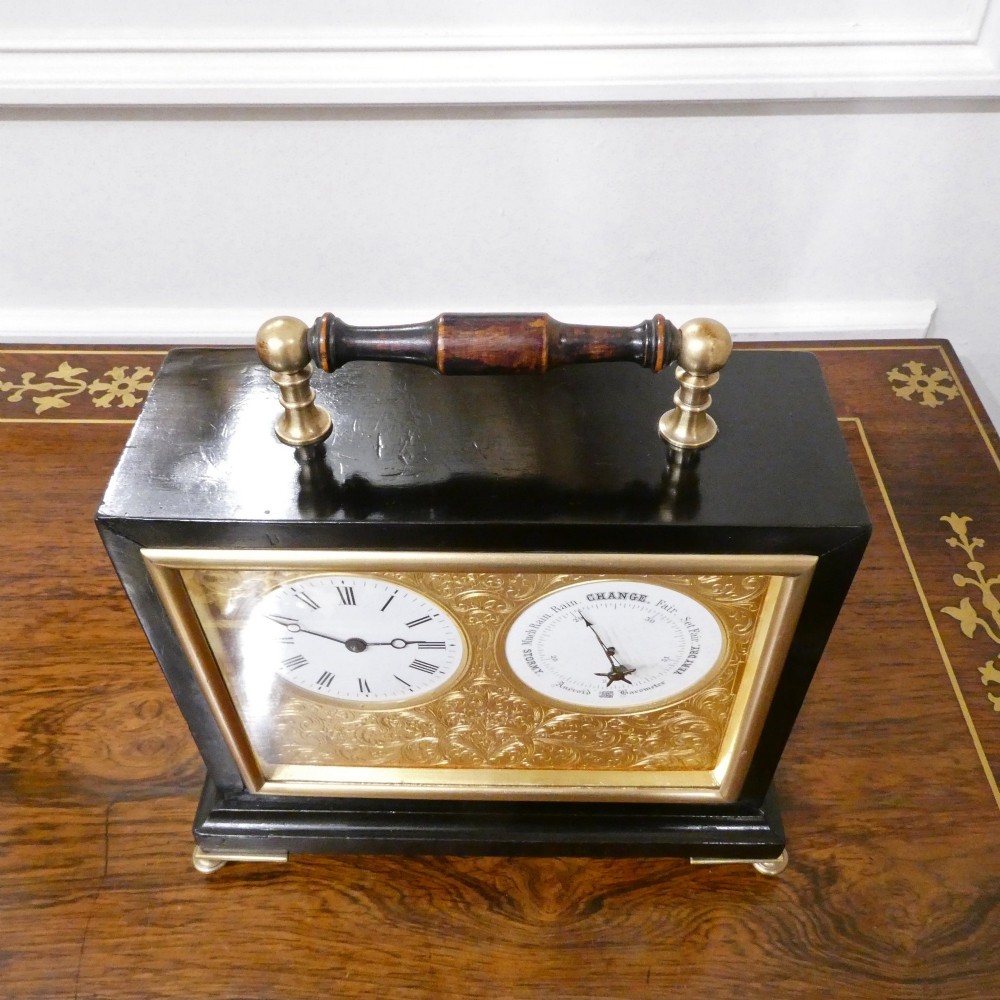 An Edwardian rectangular ebonised wooden mantel clock and barometer unit with twin white circular dials set into a scroll-engraved brass plate. View X