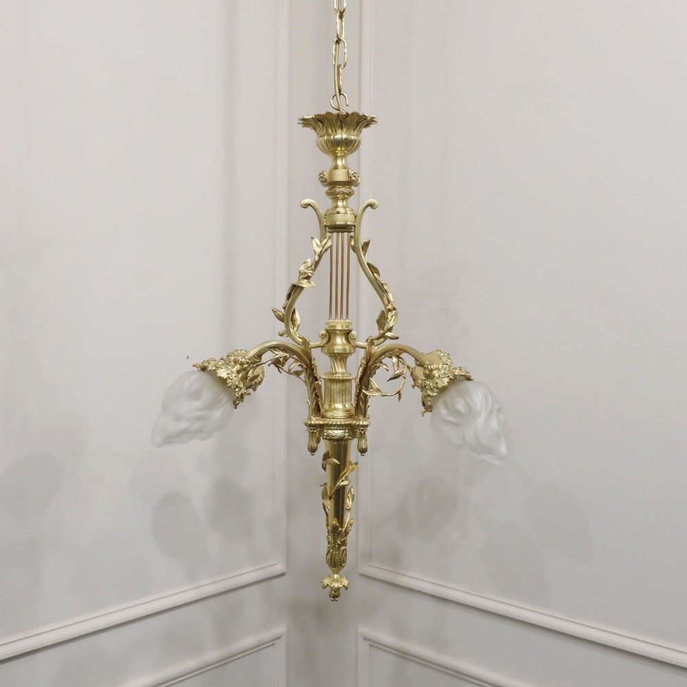 A French Neoclassical style gilt bronze chandelier featuring a central lyre-shaped stem and two outward-curving arms with frosted glass shades.