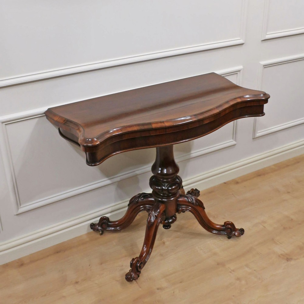 A Victorian rosewood side table featuring a serpentine fold-over top mounted on a central carved pedestal with four scroll-footed legs.