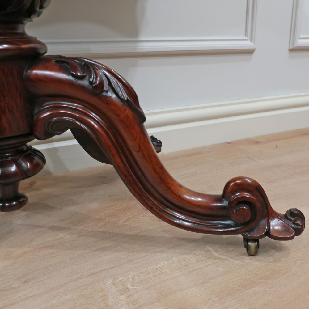 A Victorian rosewood side table featuring a serpentine fold-over top mounted on a central carved pedestal with four scroll-footed legs. View VII