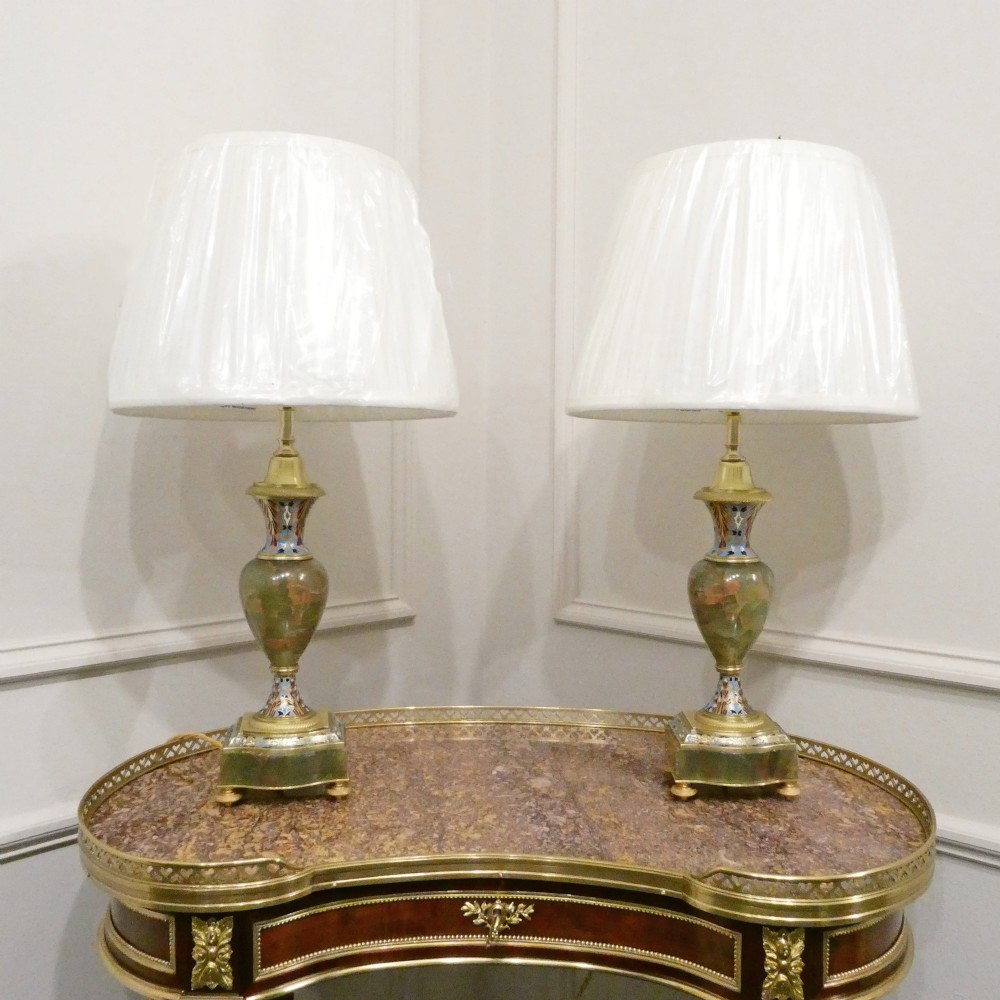 A pair of French table lamps featuring urn-shaped green onyx columns detailed with polychrome champleve enamelling and topped with pleated white shades.