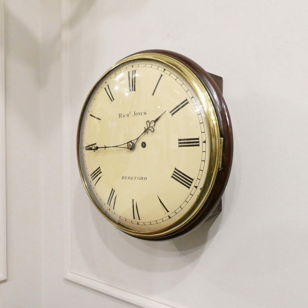 A circular Georgian wall clock featuring a cream dial with black Roman numerals, blued steel hands, a polished brass bezel, and a dark mahogany wood surround. View II