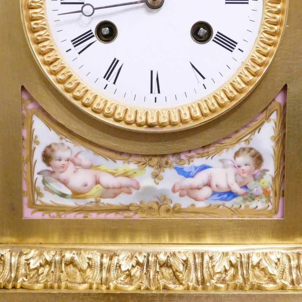 An antique French gilt bronze mantel clock featuring hand-painted pink porcelain panels, a porcelain urn finial, and an enamel dial with Roman numerals. View V