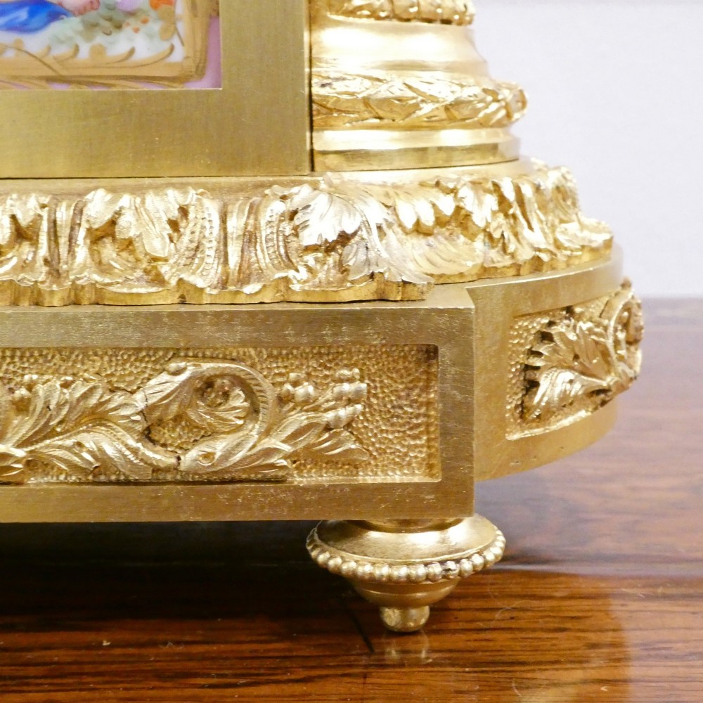 An antique French gilt bronze mantel clock featuring hand-painted pink porcelain panels, a porcelain urn finial, and an enamel dial with Roman numerals. View VI