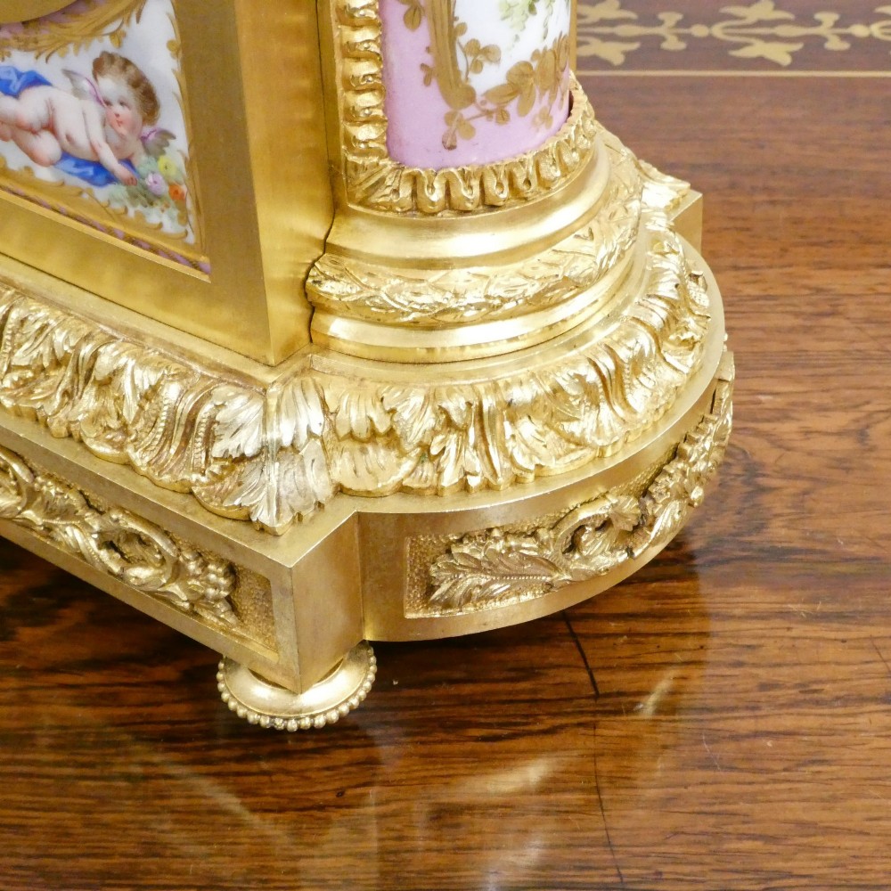 An antique French gilt bronze mantel clock featuring hand-painted pink porcelain panels, a porcelain urn finial, and an enamel dial with Roman numerals. View VII