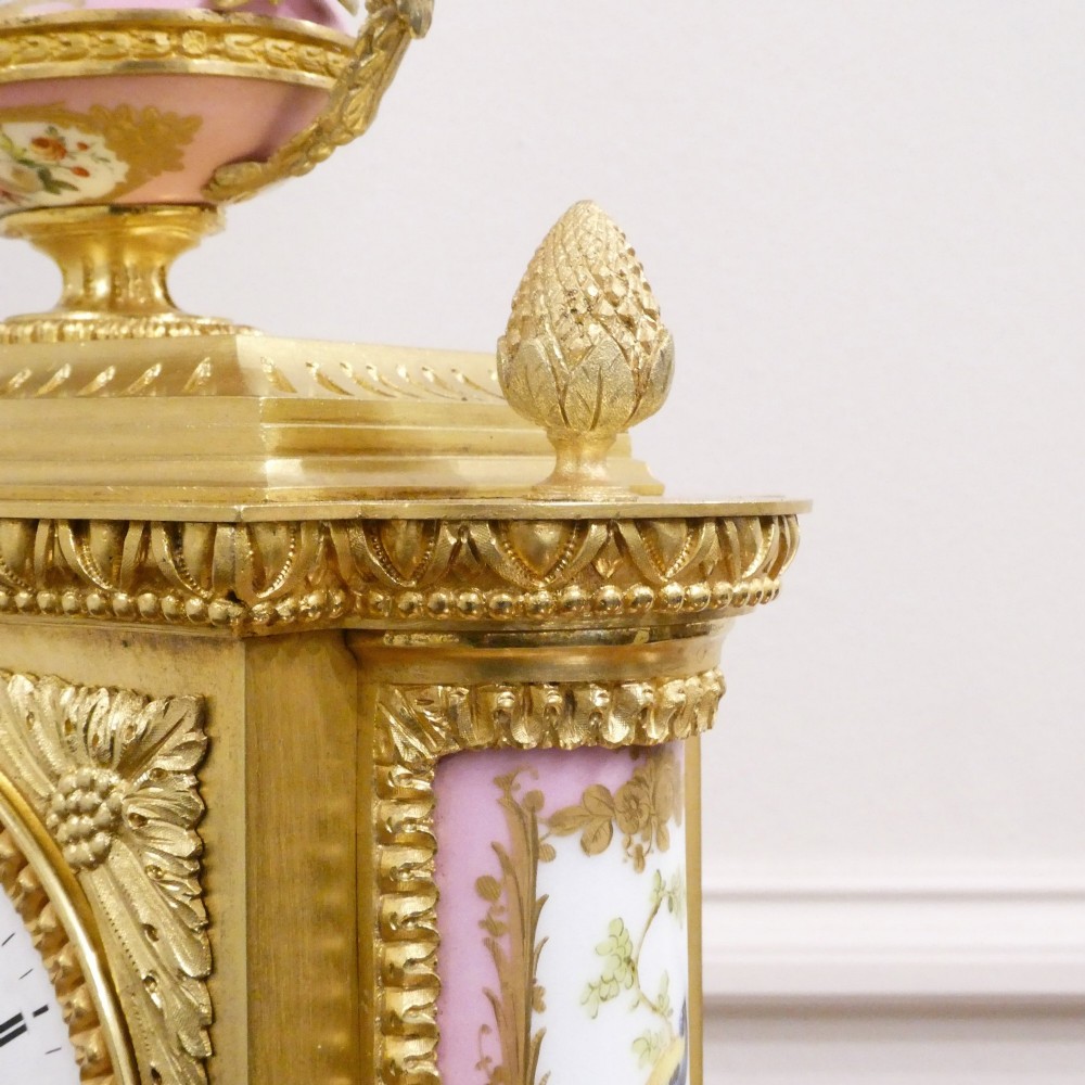 An antique French gilt bronze mantel clock featuring hand-painted pink porcelain panels, a porcelain urn finial, and an enamel dial with Roman numerals. View VIII