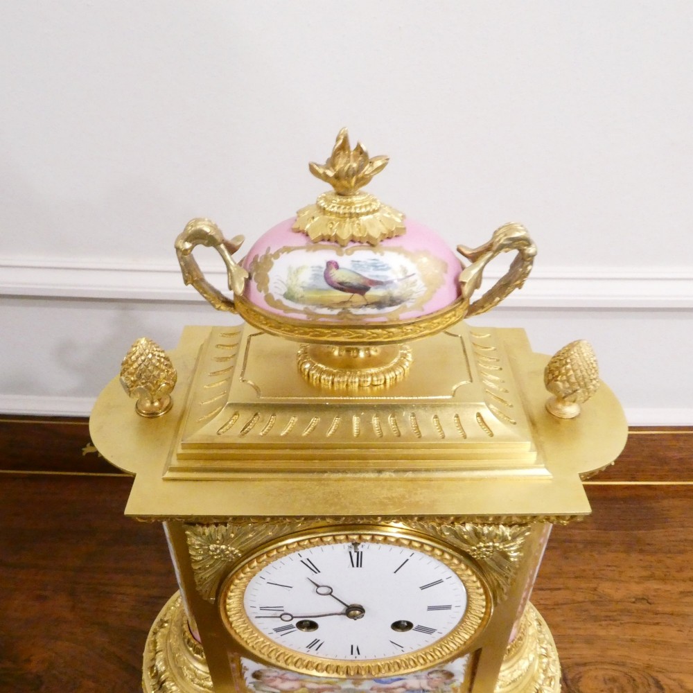 An antique French gilt bronze mantel clock featuring hand-painted pink porcelain panels, a porcelain urn finial, and an enamel dial with Roman numerals. View X