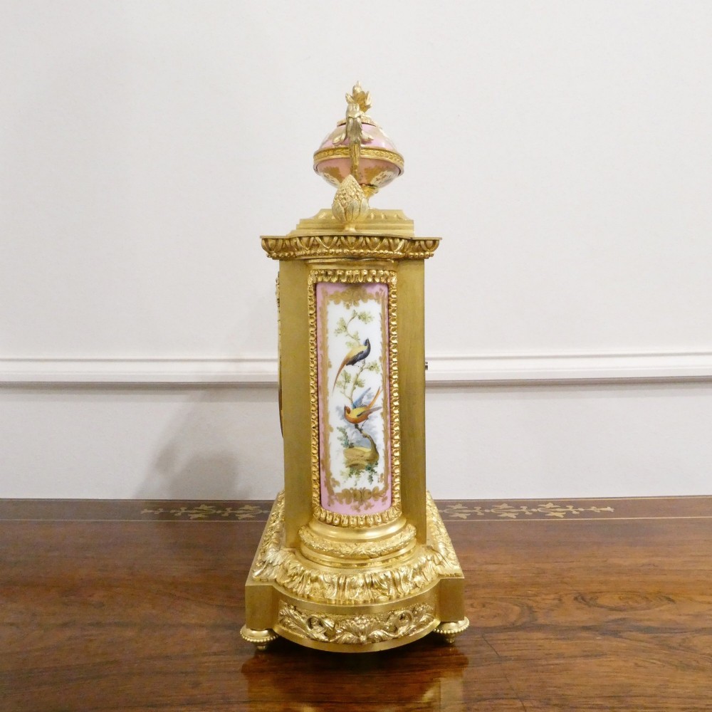 An antique French gilt bronze mantel clock featuring hand-painted pink porcelain panels, a porcelain urn finial, and an enamel dial with Roman numerals. View XII