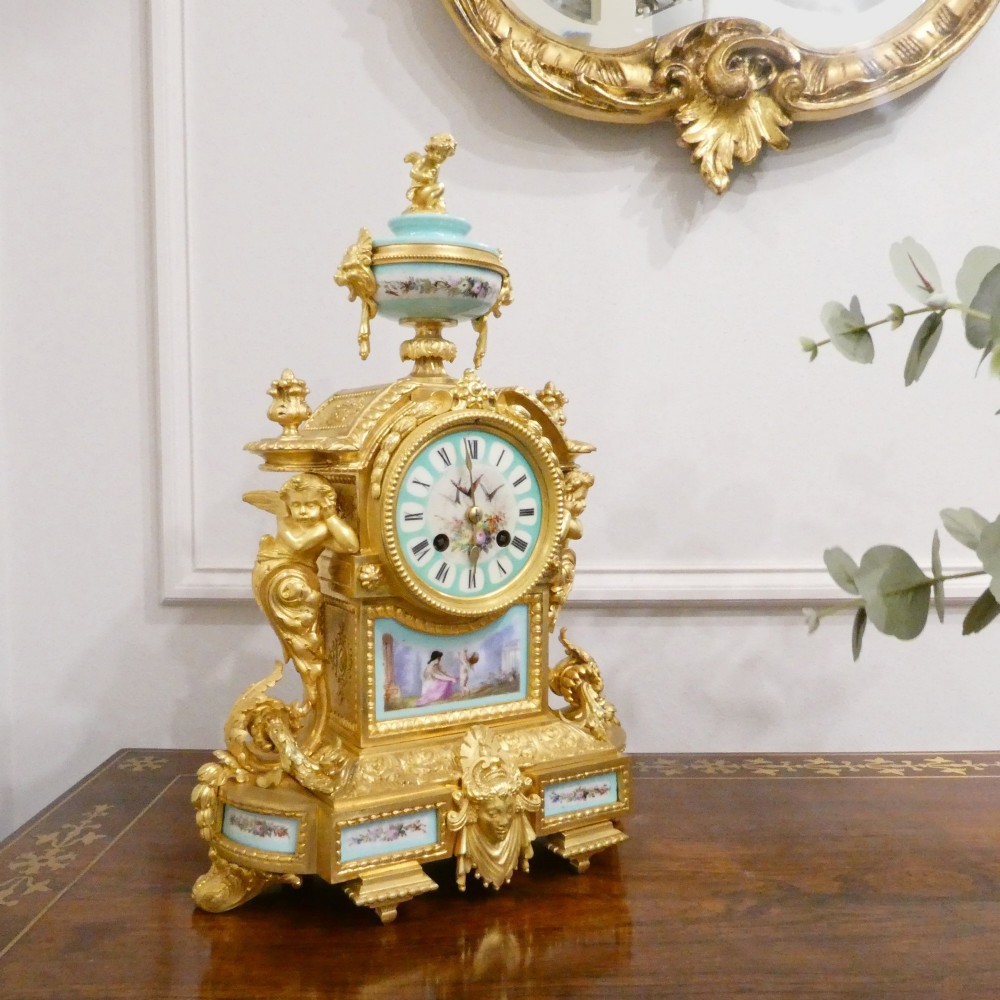 A French 19th-century gilt bronze mantel clock featuring light blue hand-painted porcelain panels, sculpted putti, an urn finial, and an enamel Roman numeral dial.