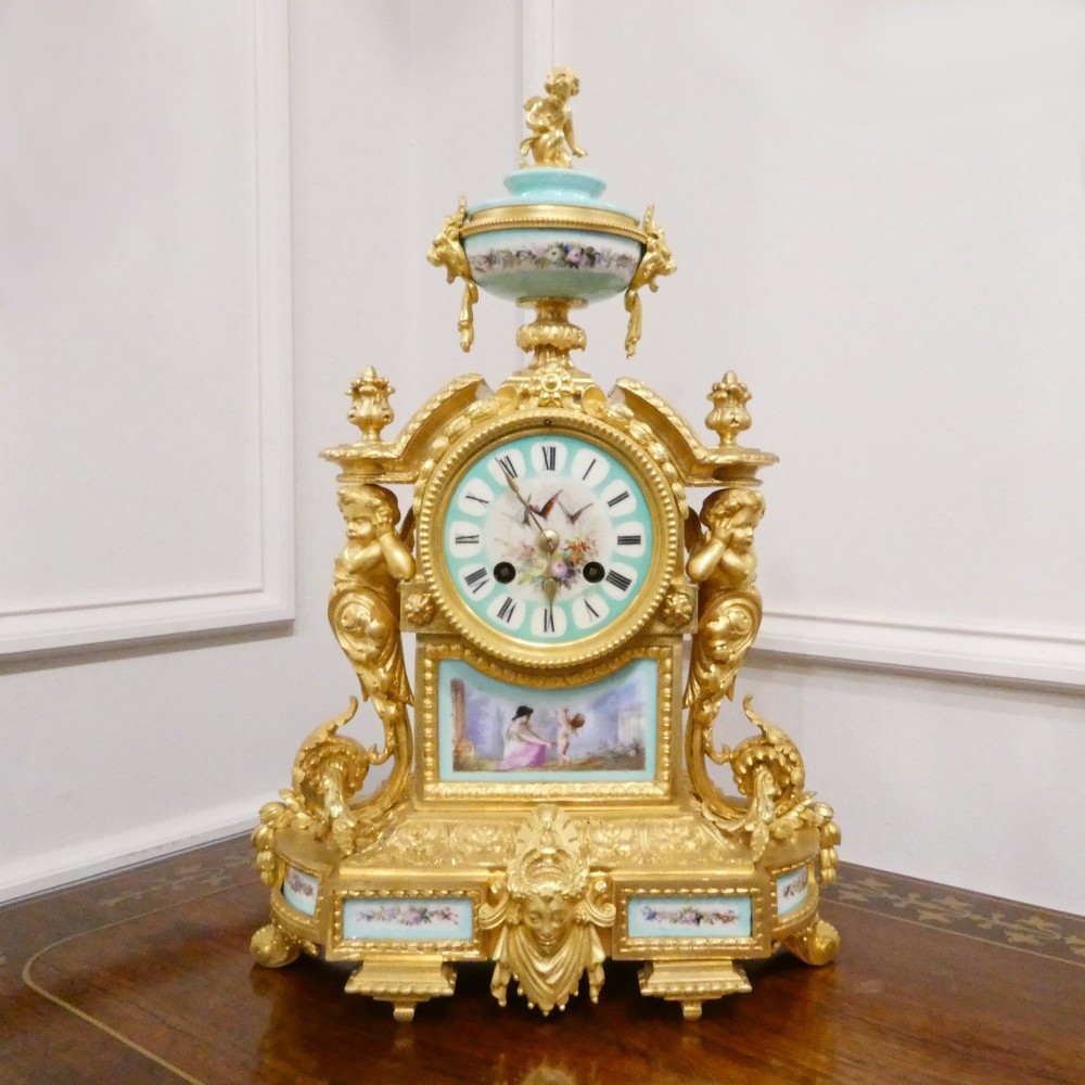 A French 19th-century gilt bronze mantel clock featuring light blue hand-painted porcelain panels, sculpted putti, an urn finial, and an enamel Roman numeral dial. View II