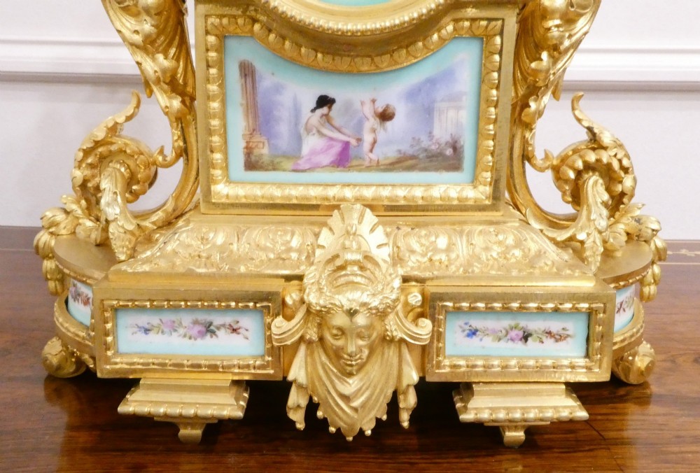 A French 19th-century gilt bronze mantel clock featuring light blue hand-painted porcelain panels, sculpted putti, an urn finial, and an enamel Roman numeral dial. View IV