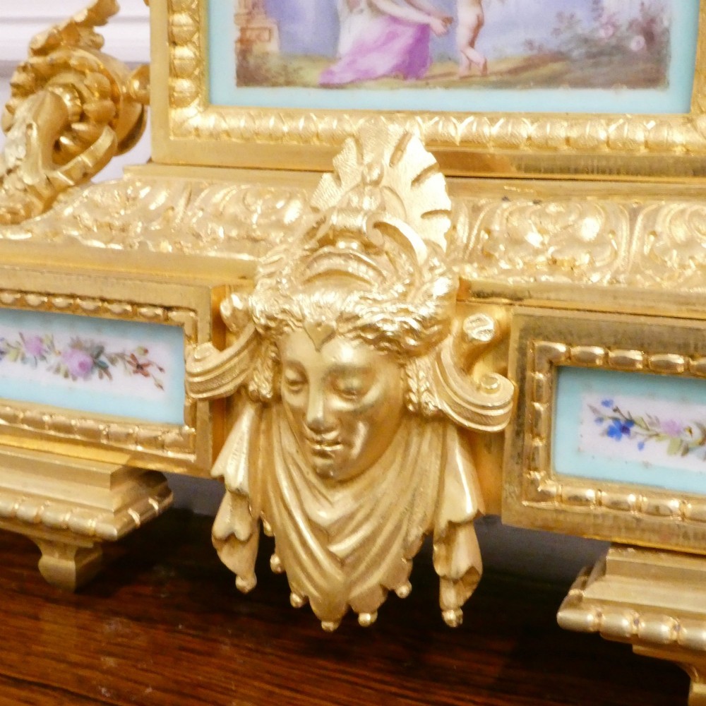 A French 19th-century gilt bronze mantel clock featuring light blue hand-painted porcelain panels, sculpted putti, an urn finial, and an enamel Roman numeral dial. View V