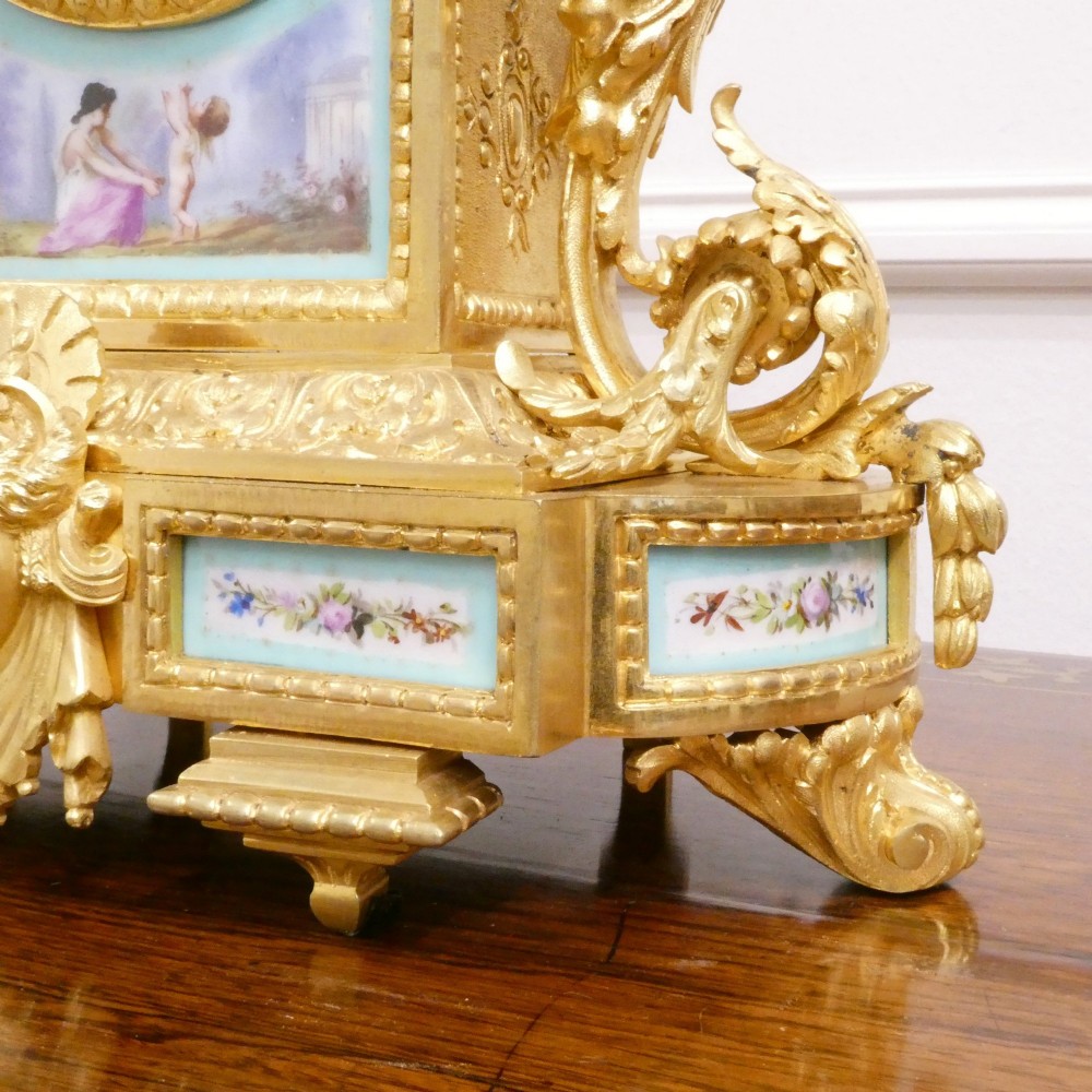 A French 19th-century gilt bronze mantel clock featuring light blue hand-painted porcelain panels, sculpted putti, an urn finial, and an enamel Roman numeral dial. View VI