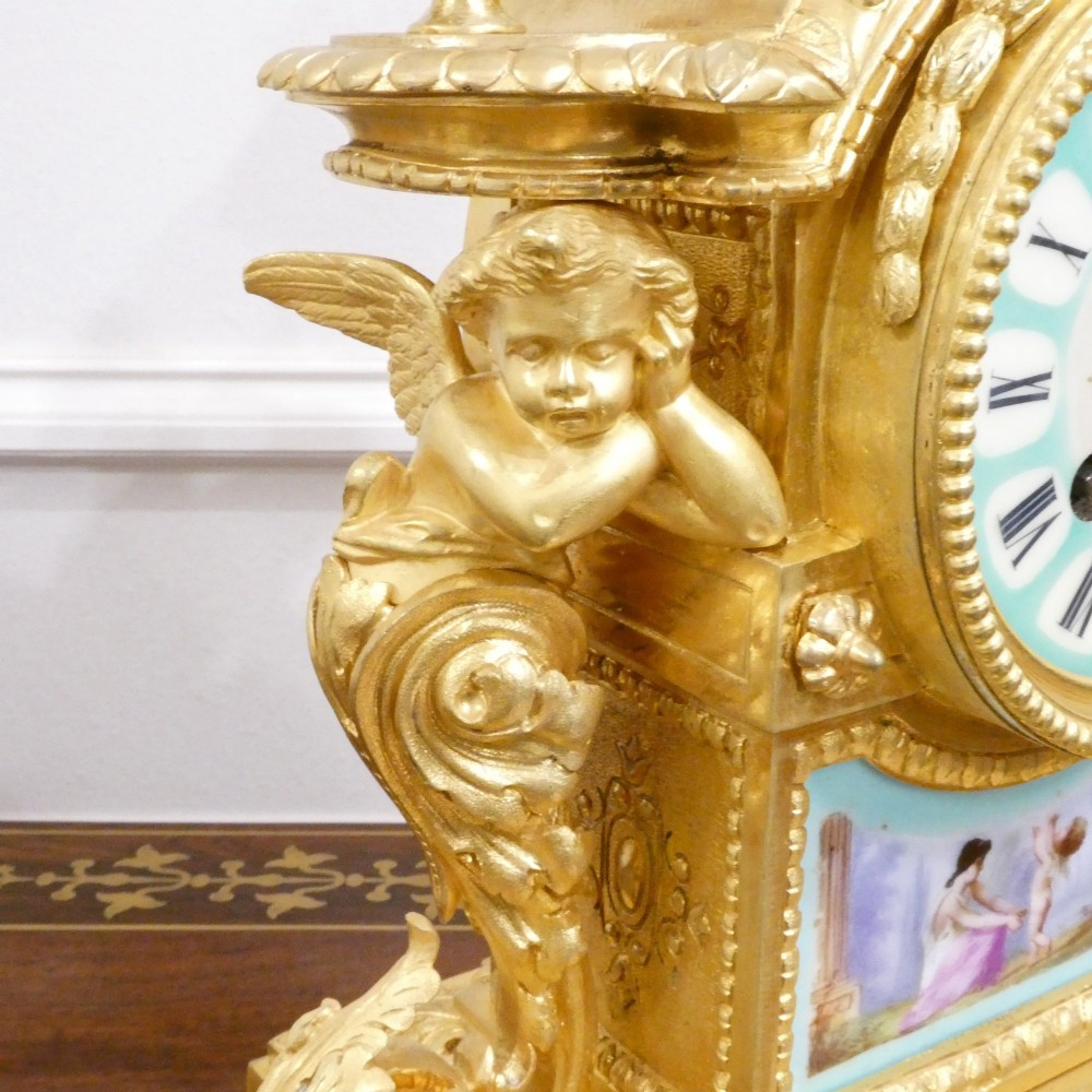 A French 19th-century gilt bronze mantel clock featuring light blue hand-painted porcelain panels, sculpted putti, an urn finial, and an enamel Roman numeral dial. View VIII