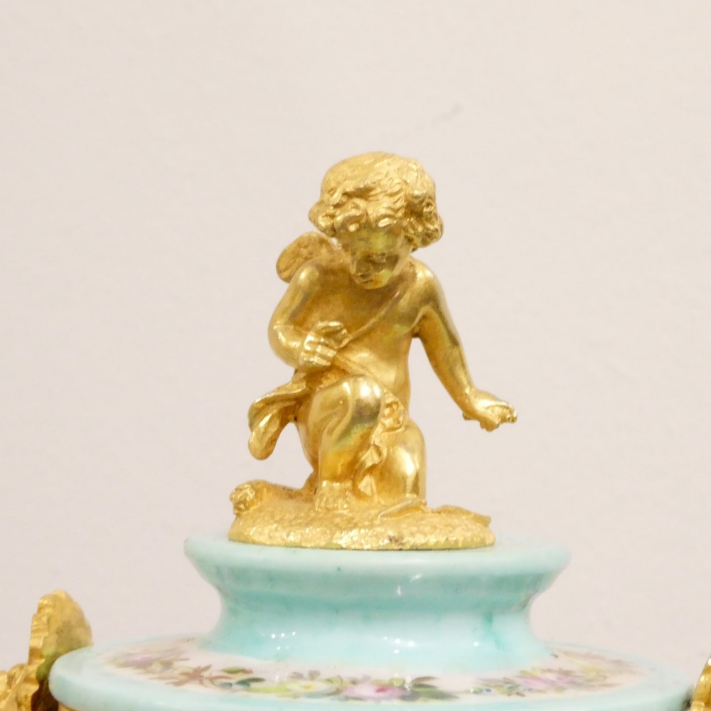A French 19th-century gilt bronze mantel clock featuring light blue hand-painted porcelain panels, sculpted putti, an urn finial, and an enamel Roman numeral dial. View XI