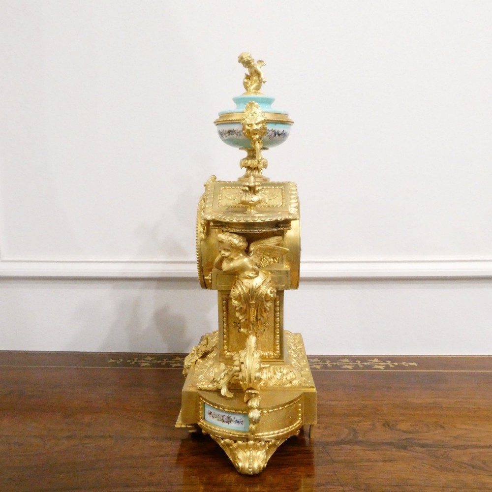 A French 19th-century gilt bronze mantel clock featuring light blue hand-painted porcelain panels, sculpted putti, an urn finial, and an enamel Roman numeral dial. View XIII