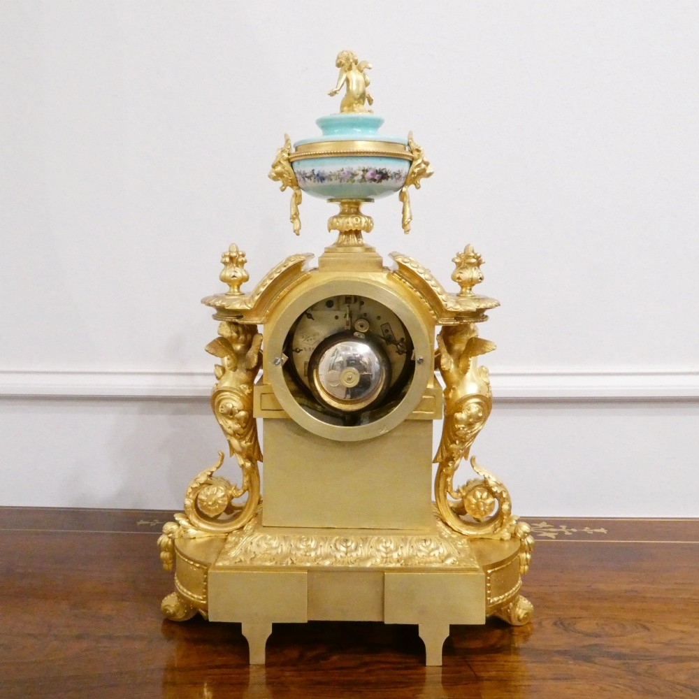 A French 19th-century gilt bronze mantel clock featuring light blue hand-painted porcelain panels, sculpted putti, an urn finial, and an enamel Roman numeral dial. View XIV
