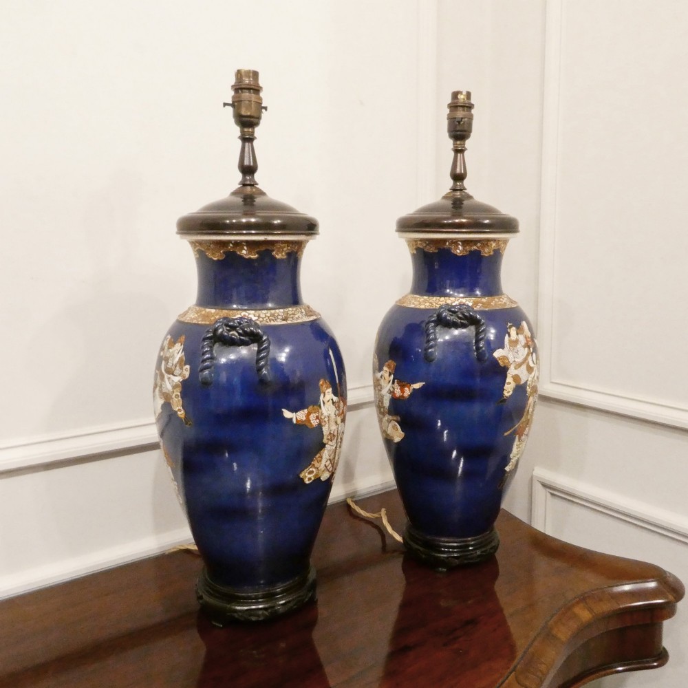 A pair of cobalt blue Japanese Satsuma porcelain table lamps decorated with gilded hand-painted figures and fitted with brass mountings and a cream pleated shade. View X