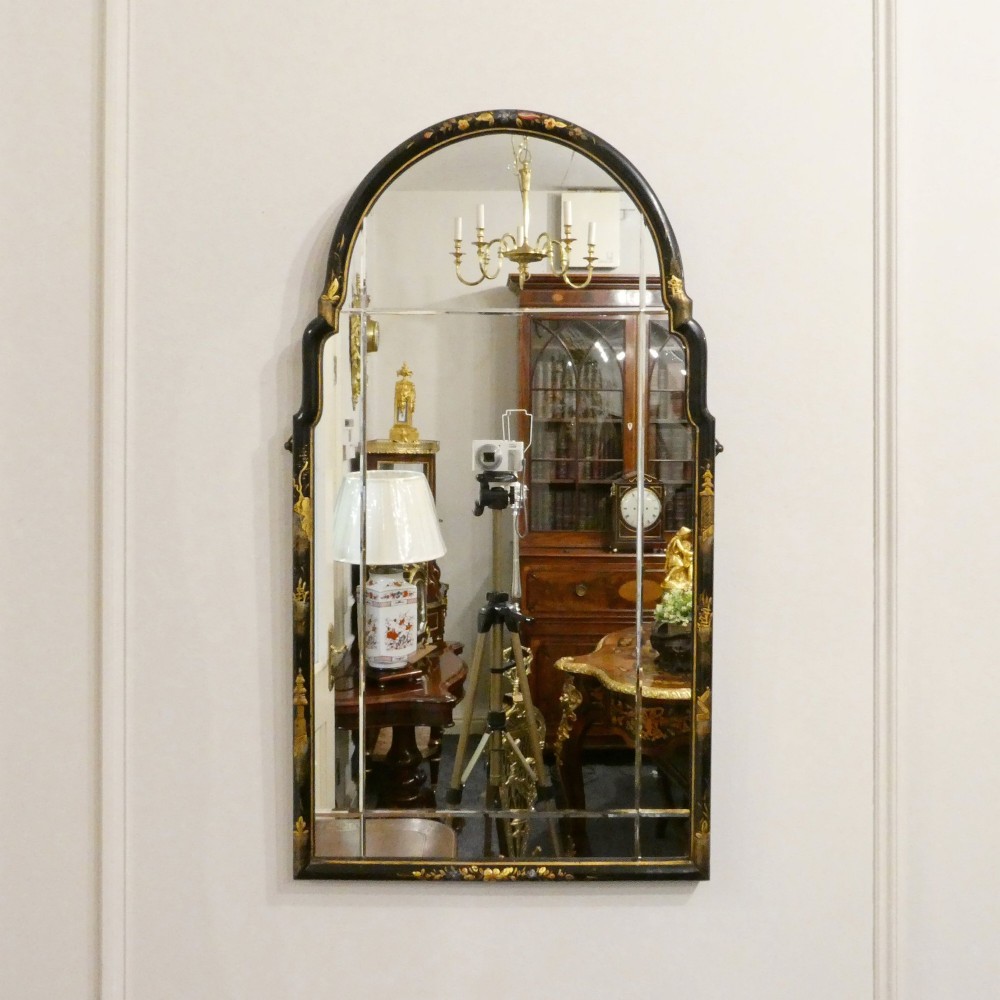 An arched wall mirror with a dark lacquered frame featuring gilded Chinoiserie motifs and segmented glass plates.