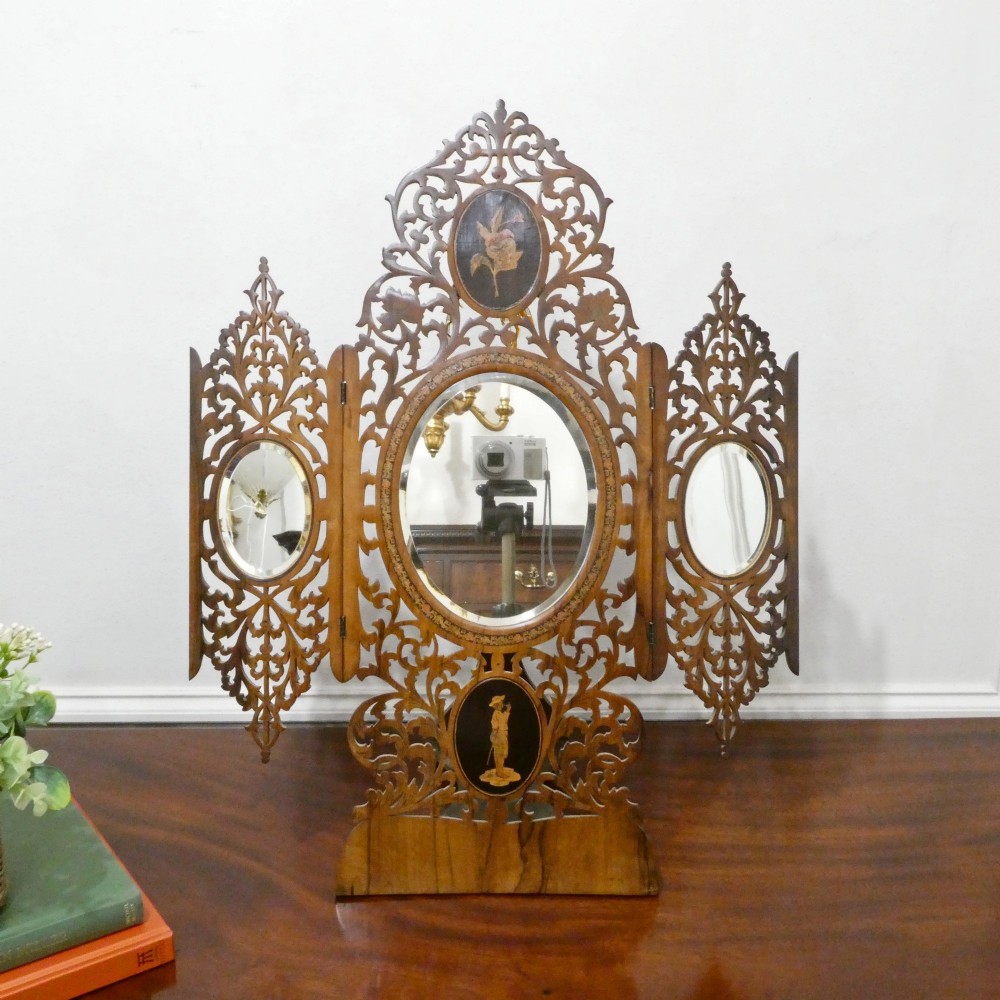 A fretted walnut triptych dressing table mirror featuring central oval glass plates surrounded by openwork carved scroll patterns and inlaid timber panels.