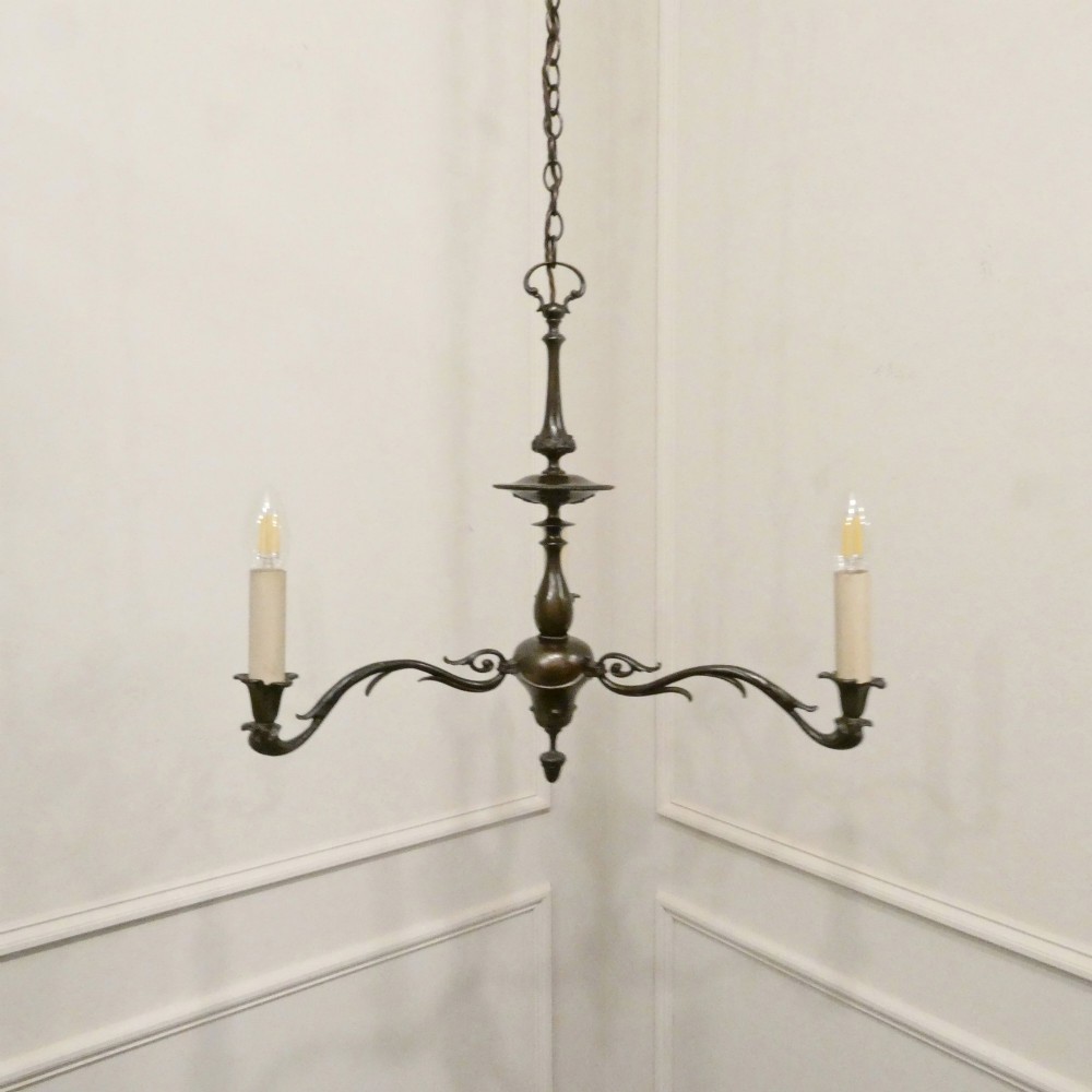 An early 20th-century Dutch bronze two-light chandelier featuring a baluster-turned central stem and curved scrolling arms.