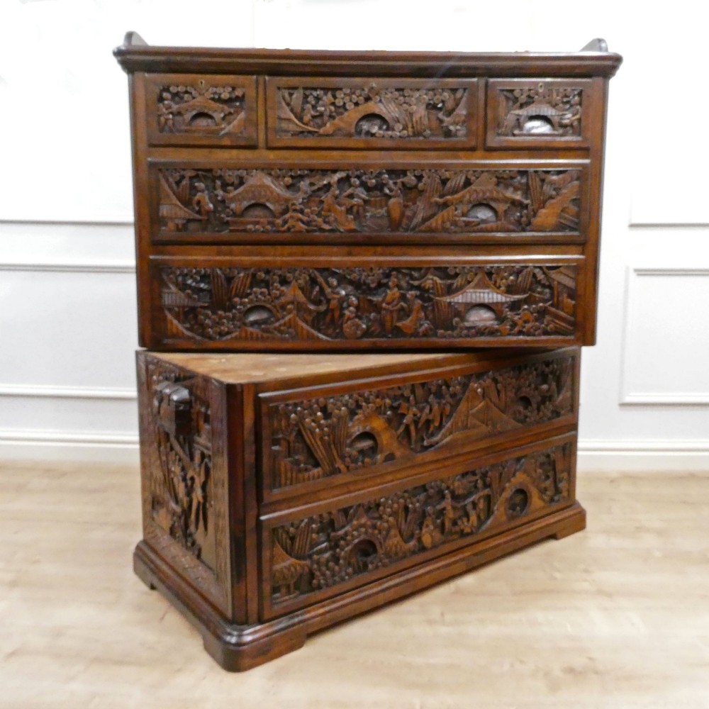 A tall early twentieth-century camphor wood chest of drawers featuring elaborate relief-carved oriental landscapes on the drawer fronts and side panels. View II