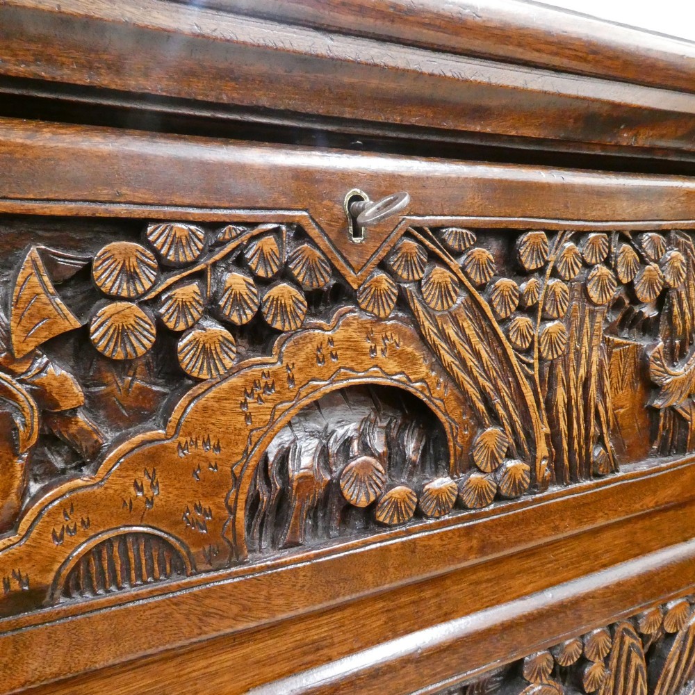A tall early twentieth-century camphor wood chest of drawers featuring elaborate relief-carved oriental landscapes on the drawer fronts and side panels. View III
