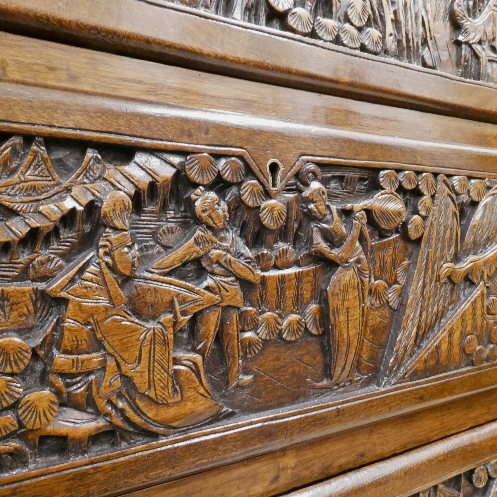 A tall early twentieth-century camphor wood chest of drawers featuring elaborate relief-carved oriental landscapes on the drawer fronts and side panels. View IV