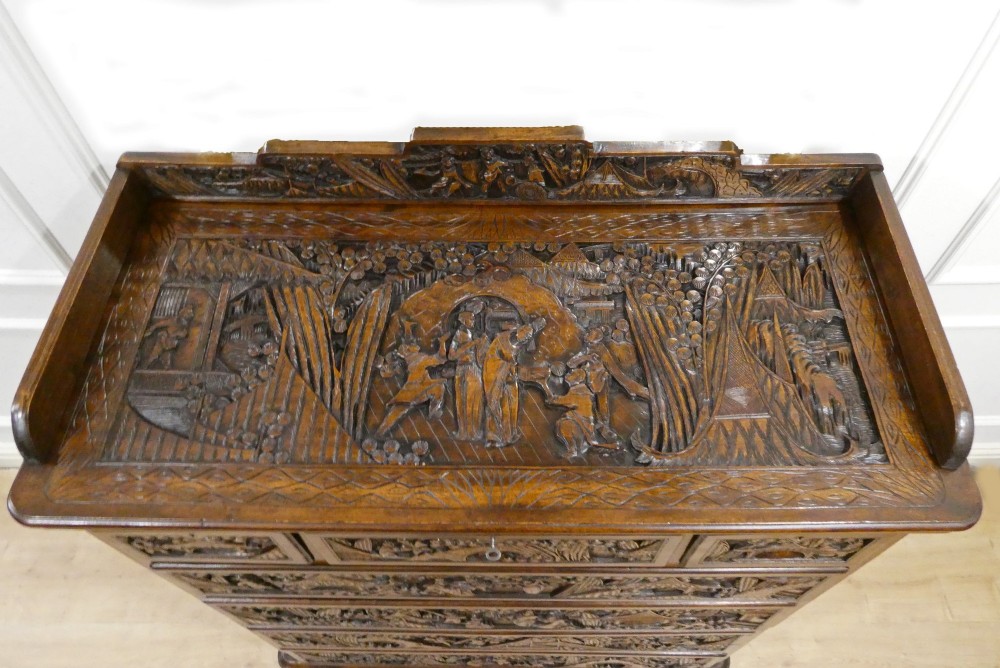 A tall early twentieth-century camphor wood chest of drawers featuring elaborate relief-carved oriental landscapes on the drawer fronts and side panels. View VI
