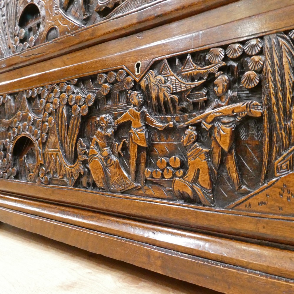 A tall early twentieth-century camphor wood chest of drawers featuring elaborate relief-carved oriental landscapes on the drawer fronts and side panels. View IX