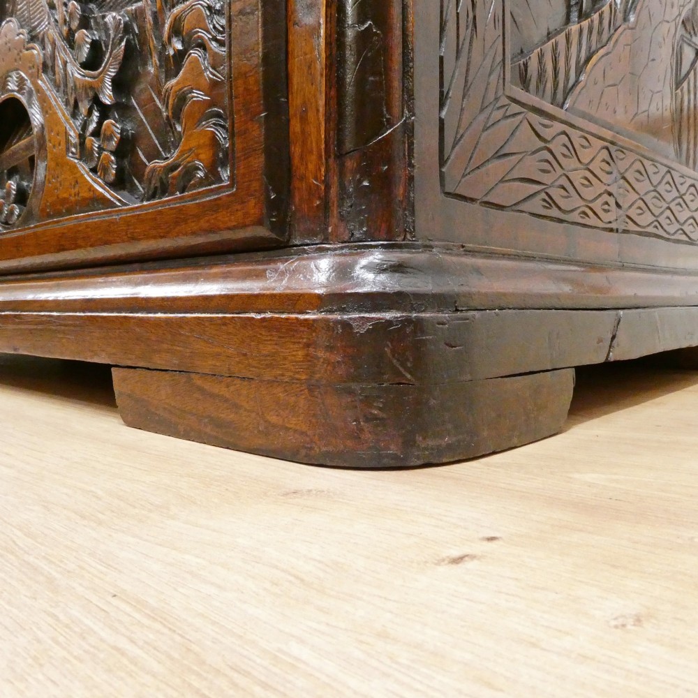 A tall early twentieth-century camphor wood chest of drawers featuring elaborate relief-carved oriental landscapes on the drawer fronts and side panels. View X