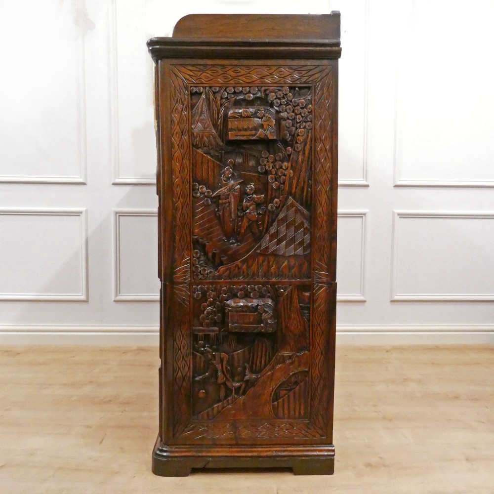 A tall early twentieth-century camphor wood chest of drawers featuring elaborate relief-carved oriental landscapes on the drawer fronts and side panels. View XI