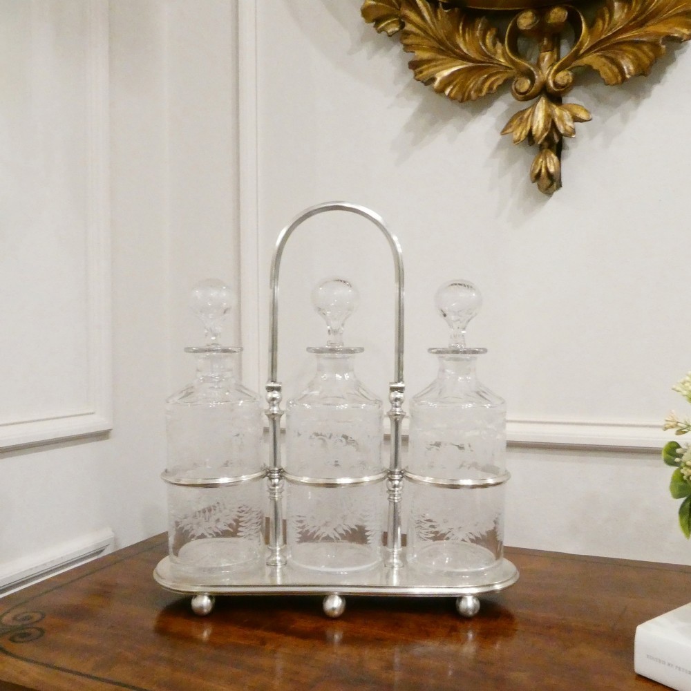 A Victorian silver-plated decanter stand with a central arched handle holding three etched glass decanters with stoppers.